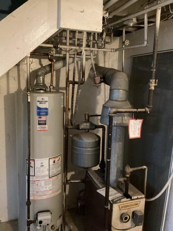 Conducted on-site assessment of Weil-McLain boiler system and Bradford White water heater installation for replacement estimate (CQ Quote: 03852-03 Boiler Est3-4p). Documented existing ductwork condition, noting worn metal ducting with multiple bends and connections, alongside PVC and copper piping configuration. System is installed in basement utility area beneath staircase with expansion tank and associated valves requiring comprehensive replacement solution.