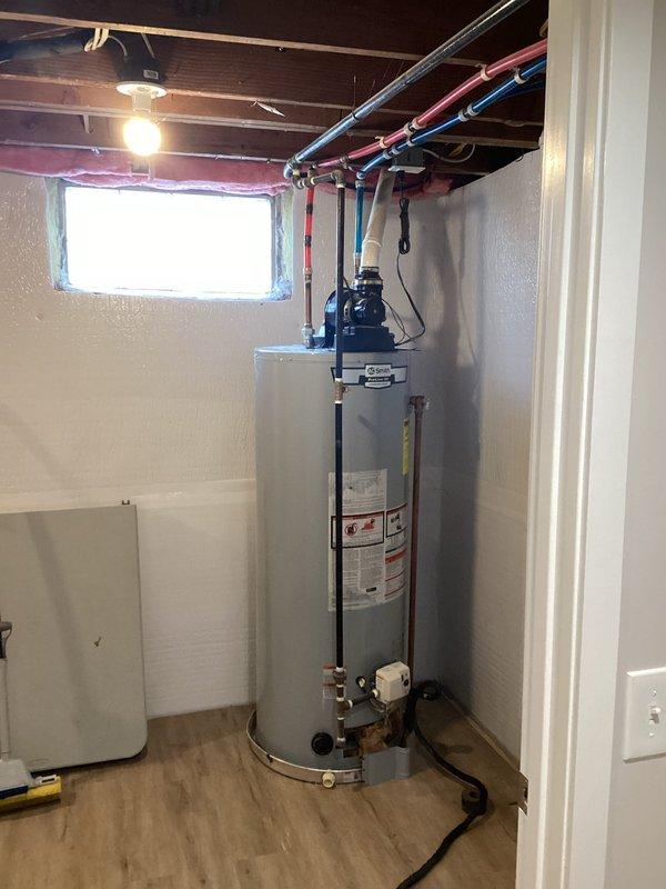 Conducted assessment of 10-year-old water heater with active leak. Unit shows signs of deterioration at connections, with water accumulation at base. System includes standard hot/cold water lines with expansion tank mounted adjacent to unit. Recommended full replacement due to age and failure of tank integrity.