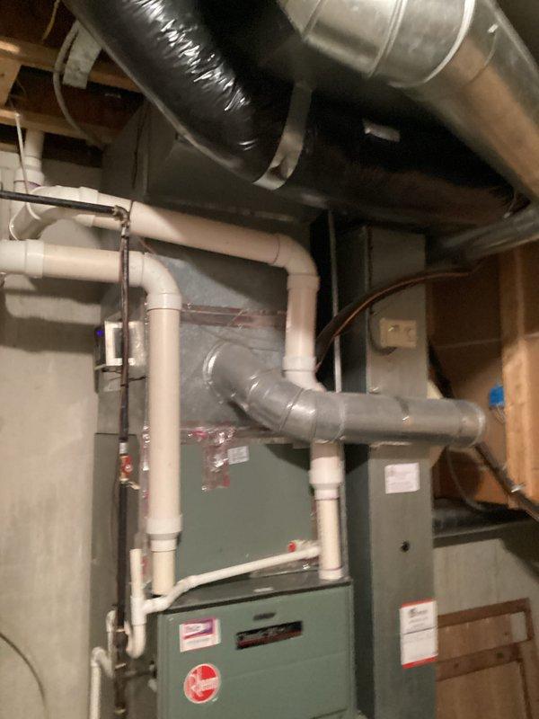 Conducted a replacement estimate for a residential furnace system located in basement utility area. Evaluated existing installation which includes green-gray furnace unit, extensive ductwork, black insulated ducting, and PVC condensate drainage system. Documented current system configuration and structural mounting to provide accurate replacement options.