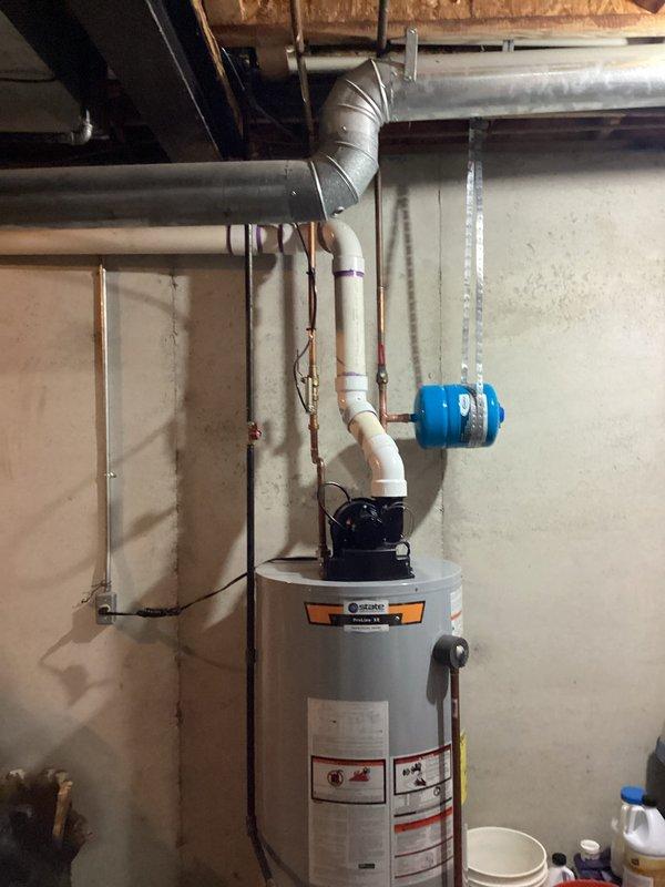 Responded to service call for intermittent dripping from discharge valve on residential water heater in basement of 32-year-old home. Upon inspection, identified temperature and pressure relief (TPR) valve discharge pipe experiencing periodic leakage over four-day period. Evaluated water heater system including circulator pump assembly, copper and PVC supply lines, shut-off valves, and venting configuration. Tested TPR valve operation and inspected for mineral buildup, sediment accumulation, and excessive pressure conditions that could cause intermittent discharge. Examined tank condition, verified proper temperature settings, and assessed overall system integrity. Checked expansion tank pressure and functionality to ensure proper thermal expansion management. Documented existing installation with photographic evidence showing gray cylindrical tank water heater with mounted circulation pump, brass fittings, red-handled shut-off valves, and proper pipe transitions from PVC to copper. Ad