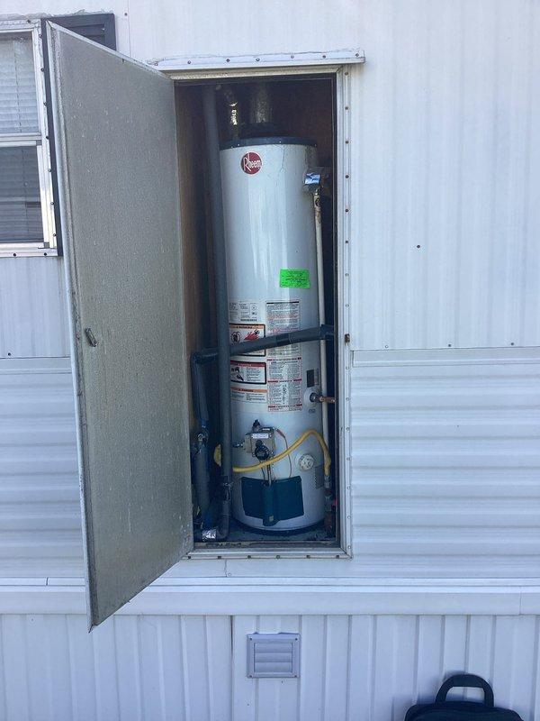 Provided comprehensive estimate for complete water heater replacement of existing Rheem residential unit currently installed in exterior access compartment with corrugated metal siding. Evaluated current installation featuring white cylindrical water heater with visible age-related deterioration on plumbing connections, including weathered bare metal piping and black foam-insulated lines. Assessment included inspection of yellow flexible gas line connector, temperature control valve, and all associated plumbing fixtures within wooden-framed utility compartment. Documented existing conditions through photographic record for replacement specifications and scope of work development.