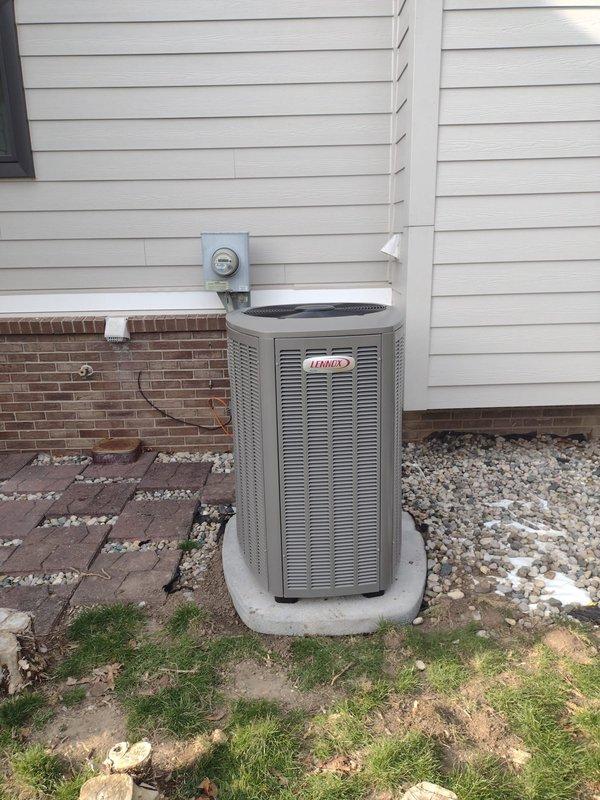 Completed full HVAC system installation including Lennox furnace, air conditioning condenser unit, humidifier, and S40 thermostat. Outdoor condenser positioned on concrete pad against exterior wall with proper electrical connections and refrigerant line routing through white conduit. Indoor furnace installed in basement mechanical room with PVC venting, integrated humidifier system, and all ductwork connections properly sealed and secured. Thermostat wired and programmed for system operation. All equipment tested and confirmed operational upon completion.