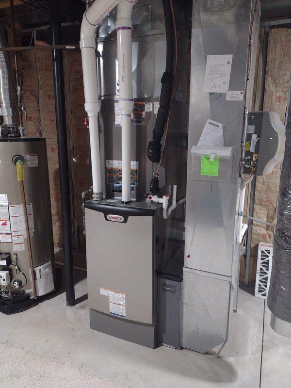 Completed full HVAC system installation including Lennox furnace, air conditioning condenser unit, humidifier, and S40 thermostat. Outdoor condenser positioned on concrete pad against exterior wall with proper electrical connections and refrigerant line routing through white conduit. Indoor furnace installed in basement mechanical room with PVC venting, integrated humidifier system, and all ductwork connections properly sealed and secured. Thermostat wired and programmed for system operation. All equipment tested and confirmed operational upon completion.