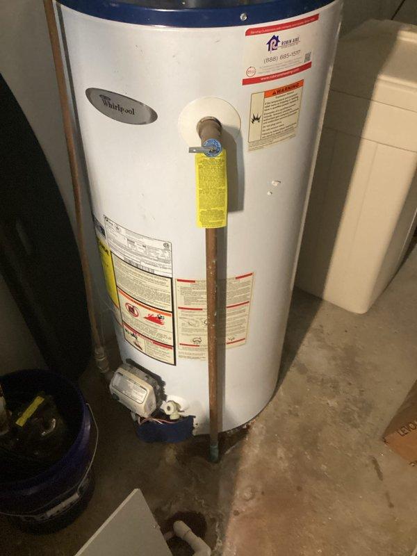 Conducted estimate for water heater replacement after identifying active leaking from aging Whirlpool unit installed in basement utility room. Documented existing equipment configuration including gas connections, copper supply lines, venting system with flexible ductwork, and proximity to water softener system for replacement planning and sizing requirements.