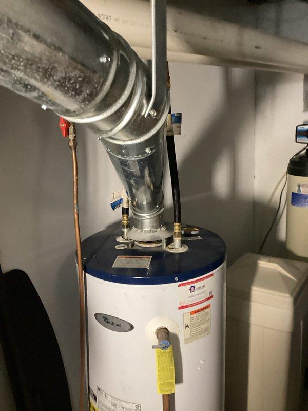 Conducted estimate for water heater replacement after identifying active leaking from aging Whirlpool unit installed in basement utility room. Documented existing equipment configuration including gas connections, copper supply lines, venting system with flexible ductwork, and proximity to water softener system for replacement planning and sizing requirements.