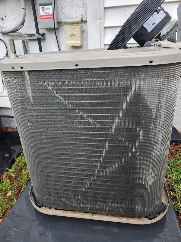 Performed annual preventive maintenance on a five-year-old residential air conditioning system located at the rear of the property. Inspection revealed heavily soiled condenser coils with significant dust and debris accumulation requiring cleaning to restore proper heat transfer efficiency. Completed comprehensive tune-up including examination of refrigerant lines, electrical connections, and compressor operation, with photographic documentation of unit condition before servicing.
