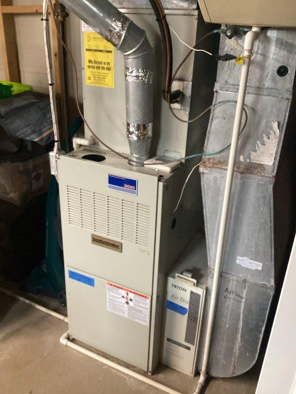 Conducted comprehensive evaluation of 27-year-old residential furnace system experiencing control board failure. Assessed existing equipment configuration including furnace unit, ductwork connections, humidifier integration, and associated refrigerant lines. Documented current system condition through detailed photography showing white cabinet-style furnace with ventilated front panel, gray metal ductwork with foil tape joints, wall-mounted humidifier unit with water line connections, and copper refrigerant piping. Provided replacement estimate options for complete HVAC system upgrade due to age of equipment and failed control board component.