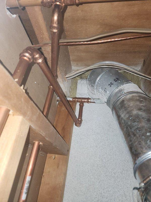 Responded to final inspection correction regarding furnace exhaust clearance violation at ceiling level. Single wall exhaust vent was found in close proximity to combustible materials including electrical wiring, failing to meet required 6-inch clearance code. Documented existing conditions with photos showing metal ductwork routing through floor joists near copper plumbing lines and electrical cables, confirming the clearance deficiency cited by inspector.