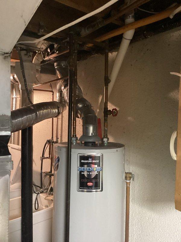 Completed comprehensive estimate for water heater replacement in residential basement utility area. Evaluated existing Bradford White Defender Safety System water heater with associated plumbing connections, including copper supply lines, PVC venting, and flexible metal ductwork. Documented current installation configuration, pipe routing along ceiling joists, and mechanical room layout. Assessed accessibility for replacement unit installation and identified necessary connections for proper integration with existing plumbing infrastructure. Photographed equipment specifications, manufacturer labels, and surrounding utility space conditions to provide accurate replacement proposal.