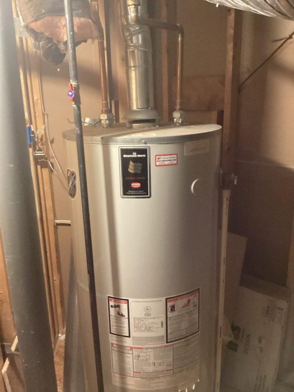 Responded to service call for non-functioning 17-year-old residential water heater that failed to ignite due to apparent corrosion damage. Conducted on-site assessment of gas-fired water heater installation in unfinished basement utility area. Inspected unit condition, verified corrosion at tank body, examined copper supply and distribution piping connections, gas line connections, temperature and pressure relief valve, and electrical/control components. Photographed existing installation showing water heater mounted on OSB platform with standard plumbing connections including cold water intake, hot water outlet, TPR valve discharge piping, and gas supply line. Documented surrounding plumbing infrastructure including vertical pipe runs and PVC venting system. Evaluated age-related deterioration and determined unit had reached end of serviceable life. Prepared comprehensive replacement estimate for new water heater installation including removal and disposal of failed unit, supply and i