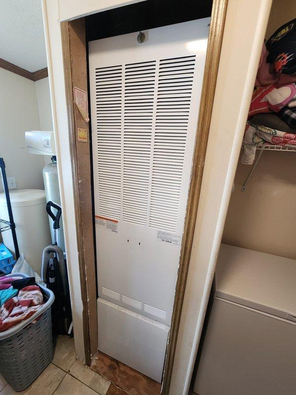 Completed full furnace installation in mobile home residential utility space. New white HVAC furnace unit installed in closet area with proper venting and clearances, secured within existing wood-framed opening adjacent to water heater. All plumbing connections, gas lines, and electrical hookups completed to manufacturer specifications and local code requirements.