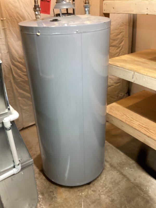 Responded to customer request for water heater replacement estimate due to reported leaking unit. Upon arrival, assessed existing cylindrical water heater located in unfinished basement utility area with exposed joists and insulation. Documented current installation including all pipe connections, copper supply lines, red-handled shutoff valve, and top-mounted fittings. Evaluated surrounding plumbing infrastructure including PVC drainage system and gas line configuration. Photographed unit positioning relative to HVAC ductwork and available clearances for replacement access. Provided comprehensive estimate for complete water heater replacement including removal of existing unit and installation of new equipment with proper venting and code-compliant connections.