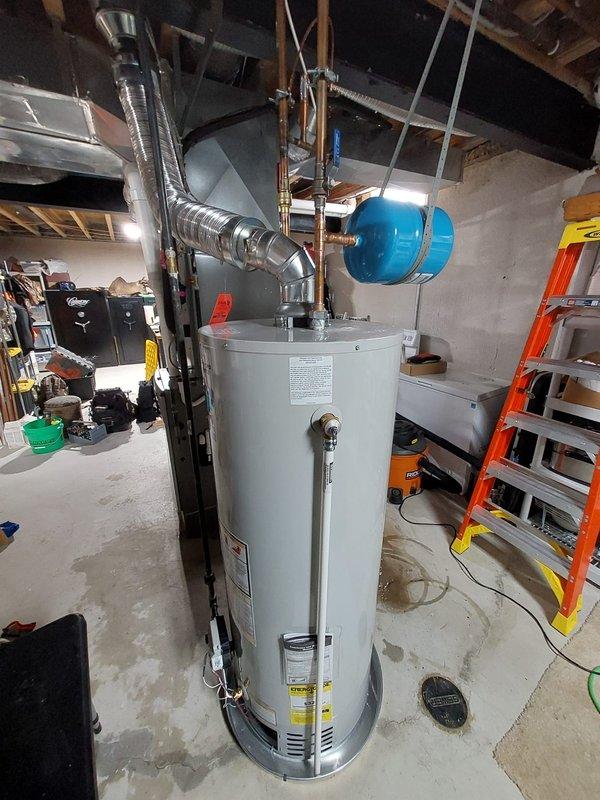 Successfully installed a new 50-gallon residential tanked water heater in the basement utility area. The installation included proper venting with flexible metal ducting, connection of copper supply lines with brass fittings and shut-off valves, and mounting of a blue expansion tank suspended from ceiling joists with metal straps. All plumbing connections were completed to code specifications, and the unit was tested for proper operation upon completion.
