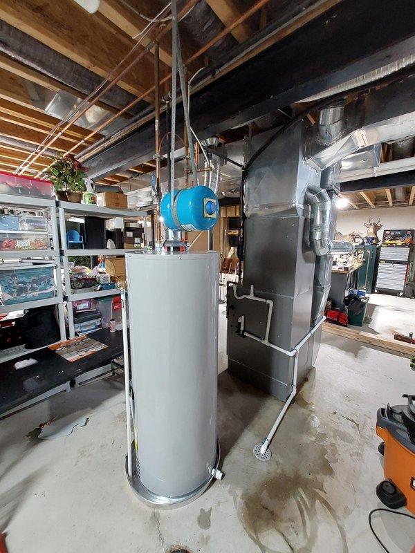 Successfully installed a new 50-gallon residential tanked water heater in the basement utility area. The installation included proper venting with flexible metal ducting, connection of copper supply lines with brass fittings and shut-off valves, and mounting of a blue expansion tank suspended from ceiling joists with metal straps. All plumbing connections were completed to code specifications, and the unit was tested for proper operation upon completion.