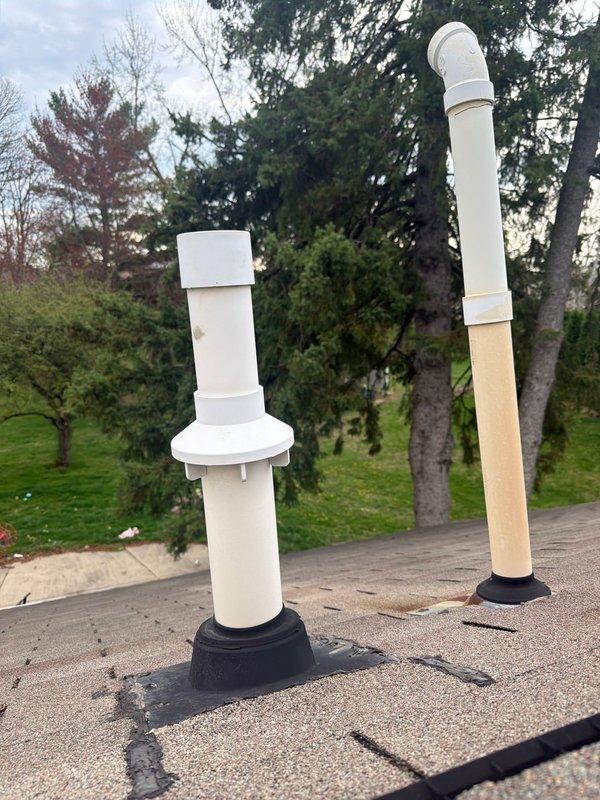 Responded to callback for exhaust intake repair on roof. Upon inspection, found two PVC vent pipe assemblies protruding from rooftop with black rubber boot seals—one shorter assembly with white cap and one taller assembly with beige middle section between white PVC segments. Verified proper sealing at roof penetrations and confirmed HVAC system operation, including furnace/air handler unit with connected ductwork and PVC condensate/vent lines. All components functioning properly with no leaks detected at roof penetrations or indoor connections.