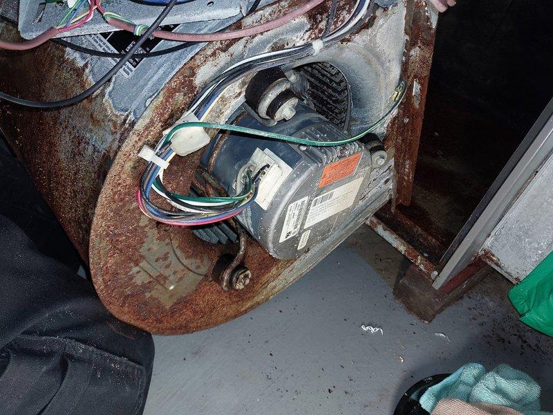 Responded to no-heat call on five-year-old furnace that had been powered off due to burning smell following water exposure in basement. Upon inspection, discovered extensive rust and corrosion throughout the blower assembly, motor mounting bracket, and surrounding metal components, indicating significant moisture intrusion. The induced draft motor, blower motor, and electrical connections showed heavy deterioration with rust covering mounting plates, brackets, and metal housing. Water damage had compromised the structural integrity of multiple components, with corrosion patterns suggesting prolonged exposure or substantial water event. 

Documented the condition of all affected components with photographs showing rust-covered motor assemblies, deteriorated mounting hardware, and compromised electrical connections. The blower motor housing exhibited severe rust penetration on the circular mounting plate and support structures. Wiring connections showed signs of moisture exposure with vi