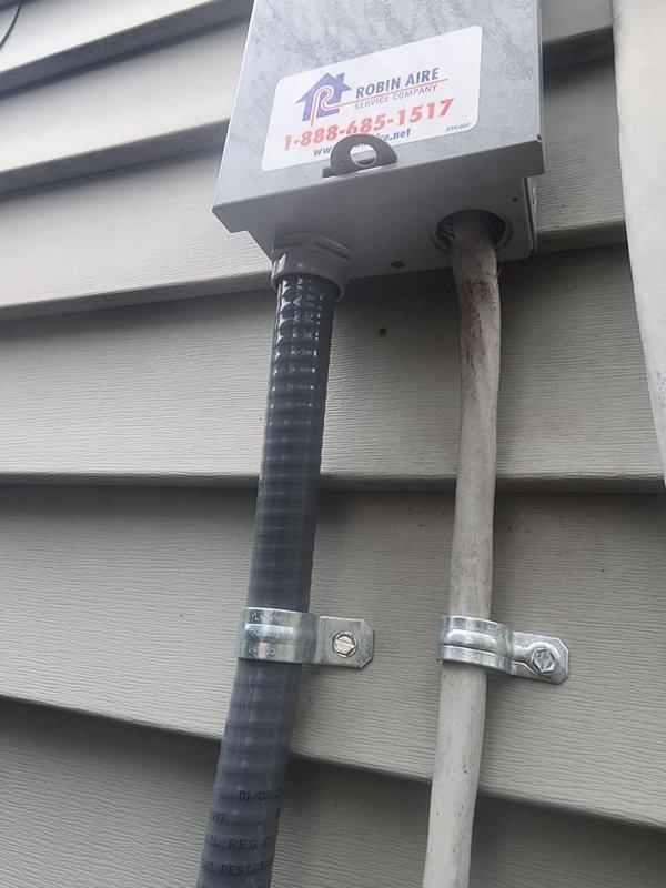 Responded to failed inspection callback to address unprotected service cable wiring at outdoor disconnect box. Upon arrival, found existing installation with black flexible conduit lacking proper connector at disconnect entry point. Installed appropriate weatherproof connector on service cable to secure and protect wiring entering the disconnect box per code requirements. Verified all electrical connections at terminal block were tight and secure, with proper wire terminations on green ground, red, and black conductors. Ensured conduit straps were properly fastened to wall and mounting plate. Installation now meets electrical code standards for exterior disconnect protection and passed re-inspection criteria.