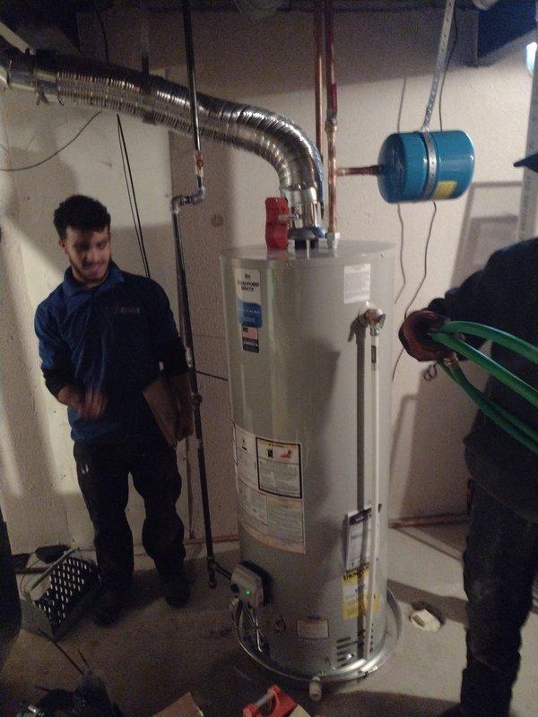 Completed installation of a 50-gallon tanked water heater in basement utility area. Installed new unit with proper connections including hot and cold water supply lines, pressure relief valve piping, and venting system using flexible metallic ductwork routed to existing exhaust path. Mounted blue expansion tank to wall with appropriate support brackets and connected to water supply system to accommodate thermal expansion. All plumbing connections secured with code-compliant fittings, and system tested for proper operation and leak-free performance.