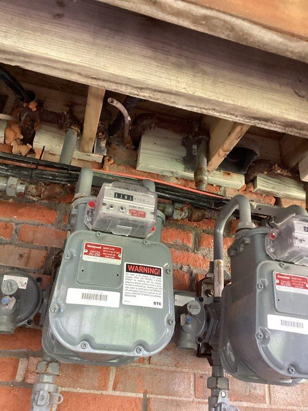 Performed on-site evaluation for air conditioning system replacement. Assessed existing R22 condensing unit located in exterior side yard area beneath elevated deck structure, noting age and condition of equipment. Documented current installation including electrical disconnect boxes, conduit routing, and unit placement on gravel pad against brick foundation. Evaluated gas meter installation in adjacent crawl space showing signs of age and corrosion on connecting pipes and fittings. Captured photographic documentation of existing equipment configuration and site conditions to support replacement estimate preparation.