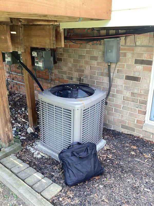 Performed on-site evaluation for air conditioning system replacement. Assessed existing R22 condensing unit located in exterior side yard area beneath elevated deck structure, noting age and condition of equipment. Documented current installation including electrical disconnect boxes, conduit routing, and unit placement on gravel pad against brick foundation. Evaluated gas meter installation in adjacent crawl space showing signs of age and corrosion on connecting pipes and fittings. Captured photographic documentation of existing equipment configuration and site conditions to support replacement estimate preparation.