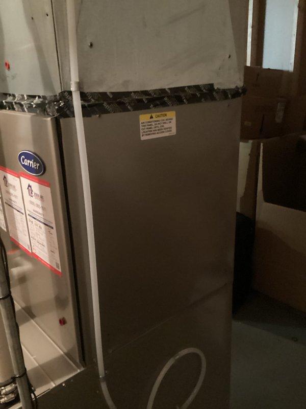 Conducted comprehensive on-site evaluation for complete HVAC system replacement at residential property. Assessed existing Carrier indoor air handler and furnace unit located in basement utility area, along with outdoor condensing unit positioned against exterior brick wall. Documented current system configuration including multi-zone split system setup with multiple refrigerant line sets penetrating building envelope. Photographed indoor equipment installation showing metal cabinet units with connecting ductwork in unfinished basement space with exposed framing. Evaluated outdoor condenser unit condition, noting white/beige cabinet with protective grilles, existing electrical disconnect box, and refrigerant line routing through brick wall penetrations. Captured images of installation environment including PVC drainage piping, flexible ductwork connections, and equipment placement relative to structural elements. Provided detailed photographic documentation of both indoor and outdoor c