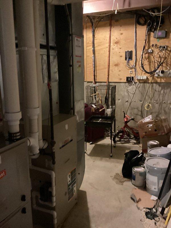 Conducted comprehensive on-site evaluation of existing HVAC system in basement utility area for R-22 refrigerant-based air conditioning replacement estimate. Assessed current furnace, air handler configuration, and associated ductwork connections, documenting equipment age, condition, and installation specifications. Photographed existing beige furnace unit with adjacent HVAC components, white PVC condensate drainage system, water heater proximity, and available workspace for potential equipment replacement, noting concrete floor installation area and electrical service accessibility for future system upgrade recommendations.