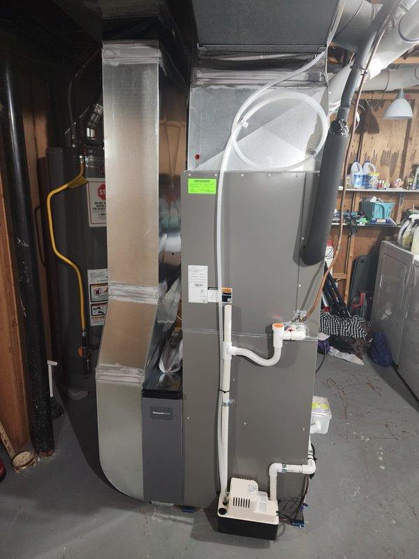 Completed installation of new Lennox high-efficiency furnace in residential basement utility area. Unit was positioned on concrete floor and connected to existing rectangular sheet metal ductwork system with proper sealing and support. White PVC condensate drainage lines were installed and secured with appropriate fittings to ensure proper moisture removal from the system. Yellow gas supply line was connected to furnace per manufacturer specifications and local code requirements. All ductwork connections were completed, including large rectangular supply plenum and flexible ducting to distribution system. Condensate pump assembly was installed at base of unit for proper drainage management. Verified all electrical connections, tested ignition sequence, and confirmed proper airflow through supply and return ducts. System was commissioned and tested for safe operation, with all safety controls functioning as designed.