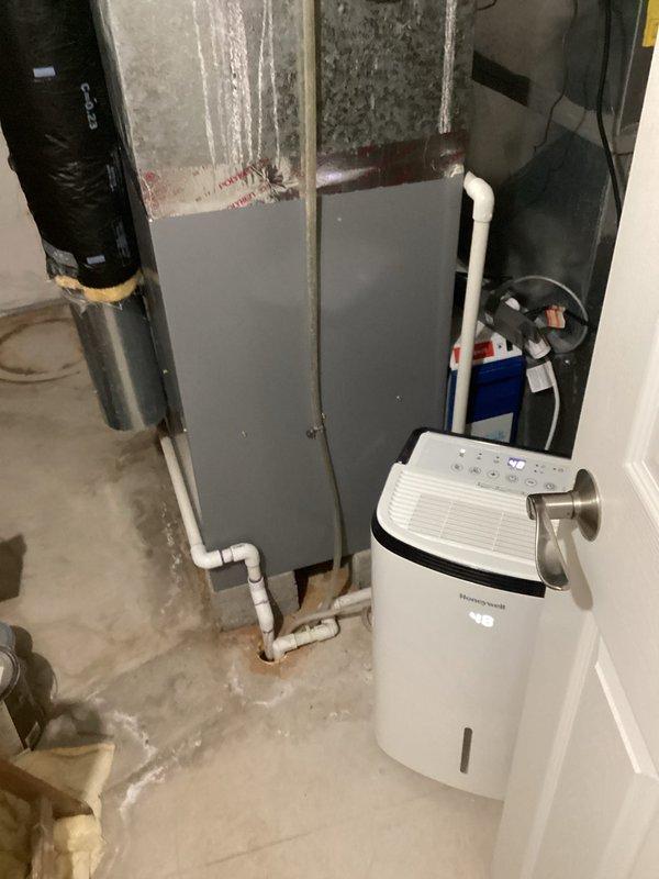 Conducted comprehensive assessment of existing HVAC system in basement utility area for equipment replacement estimate. Evaluated current gray metal air handler unit with connected PVC drainage piping, documented equipment specifications and installation configuration. Inspected surrounding mechanical room conditions including concrete block foundation walls, floor moisture conditions, and available clearances for new equipment installation. Photographed existing system layout, utility connections, and spatial constraints to develop accurate replacement proposal for complete HVAC system upgrade.