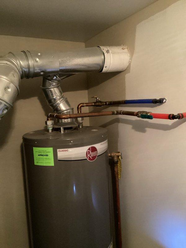 Completed comprehensive assessment and generated estimate for water heater replacement in Building 1, Unit 11-1. Evaluated existing Rheem Classic residential water heater installation including all associated plumbing connections, venting system, and safety components. Documented current configuration showing standard residential setup with copper supply lines, red and blue handled shut-off valves, expansion tank mounted at top of unit, metal venting ductwork, flexible hose connections, and proper drain pan installation at base. Photographed all mechanical connections, safety labels, and existing equipment specifications to provide accurate replacement estimate for client consideration.