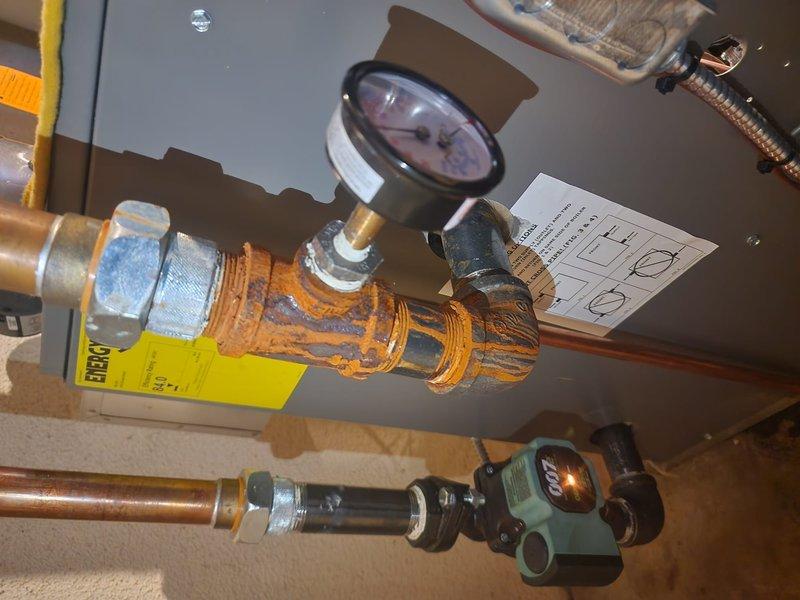 Responded to emergency no-heat call for six-month-old boiler system experiencing dangerously high pressure exceeding 50 psi with active water leakage and visible corrosion on copper piping. Upon arrival, found unit already shut down by customer due to safety concerns. Inspection revealed severe rust and corrosion on multiple copper pipes near the pressure relief system, with pressure gauge confirming excessive system pressure. Identified compromised pressure relief valve and corroded piping as primary failure points requiring immediate attention to prevent potential vessel rupture. Documented extensive corrosion on copper supply lines and fittings, noting unusual degradation for equipment of this age. System was photographed for warranty documentation showing corroded pipes, malfunctioning pressure gauge, and compromised brass fittings throughout the boiler assembly. Recommended immediate replacement of affected components and full system pressure testing before restoration of service 