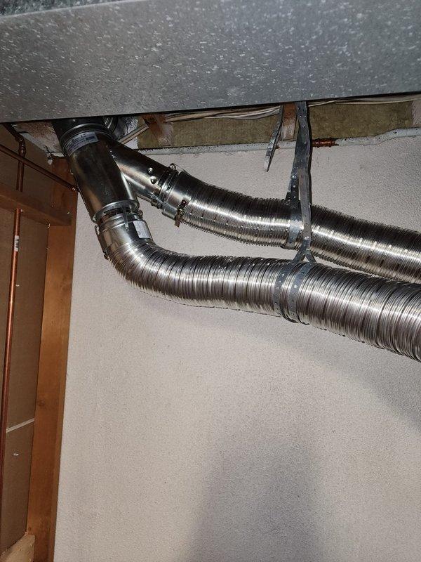 Responded to callback for furnace exhaust code compliance issue. Inspected single-wall exhaust ductwork at ceiling level and verified clearance measurements to combustible materials and electrical wiring. Documented existing conditions with photographs showing flexible metallic ductwork installation, transition fittings, and proximity to ceiling joists and insulation. Completed follow-up documentation for reinspection scheduling to ensure 6-inch clearance requirements are met per code specifications.