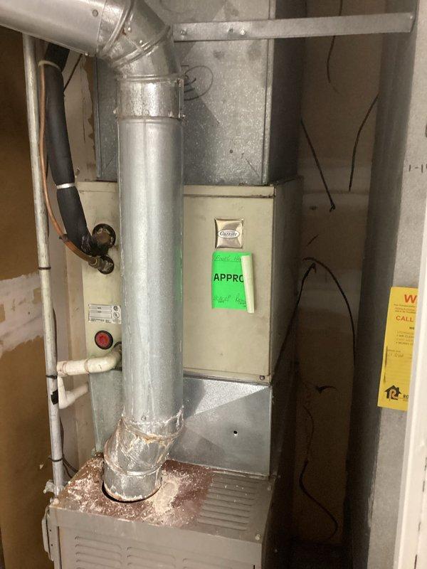 Conducted comprehensive site assessment for commercial HVAC system replacement, documenting existing Carrier furnace installation in interior mechanical space and outdoor condensing unit positioned between building structures. Photographed current equipment configuration, ductwork routing, utility connections including PVC condensate lines and electrical service, and outdoor unit placement in mulched area adjacent to brick exterior wall to develop accurate replacement specifications and installation requirements.