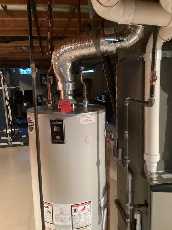 Conducted on-site assessment for water heater replacement in basement of 26-year-old residential property. Inspected existing gas-fired water heater installation, documenting current unit configuration, venting system with metallic flexible duct, copper supply piping with shutoff valves, and PVC drain connections. Evaluated utility room layout, clearances, and existing plumbing infrastructure to determine replacement specifications and installation requirements. Photographed equipment, piping connections, gas valve assembly, and surrounding HVAC components to prepare comprehensive replacement estimate.