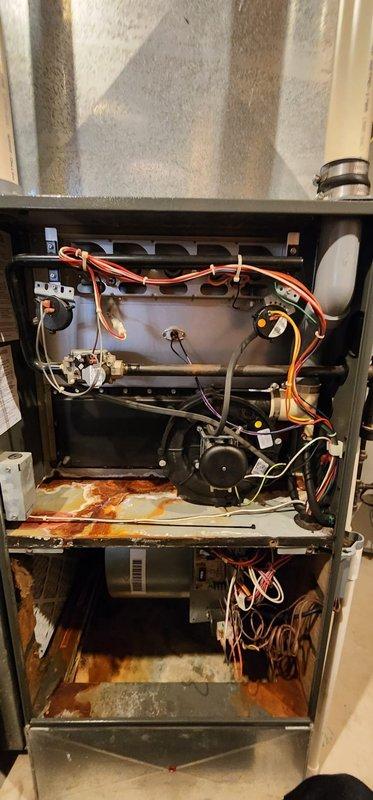 Completed scheduled furnace maintenance on residential forced-air heating system. Upon inspection, discovered significant rust and corrosion throughout the interior components, particularly on the lower compartment floor and base plate, indicating moisture exposure and age-related deterioration. Performed standard maintenance procedures including inspection of heat exchanger assembly, blower motor, electrical connections, and ductwork connections. Documented equipment condition with photographs for service records, noting the extensive rust damage on metal surfaces and internal components that may require future attention or replacement.