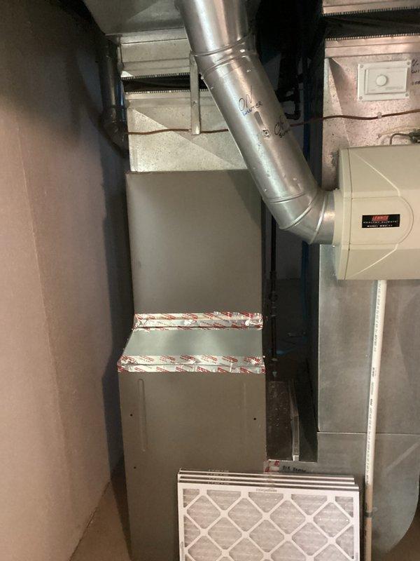 Conducted comprehensive site evaluation for complete HVAC system replacement at residential property. Assessed existing Coleman furnace unit, ductwork configuration, and current air filtration system in basement utility area. Documented equipment specifications, spatial constraints, and existing infrastructure including metallic supply ductwork with angular connections and wall-mounted air purification device. Evaluated furnace condition noting sealed horizontal seam with barrier tape, standard air intake with diamond lattice filter, and proper clearances within unfinished space. Photographed secondary mechanical area showing water heating equipment and dark ductwork distribution system with exposed framing and insulation. Compiled measurements and technical specifications necessary for preparing accurate replacement estimate including equipment sizing requirements, ductwork modifications, and installation logistics for proposed air conditioning system integration.
