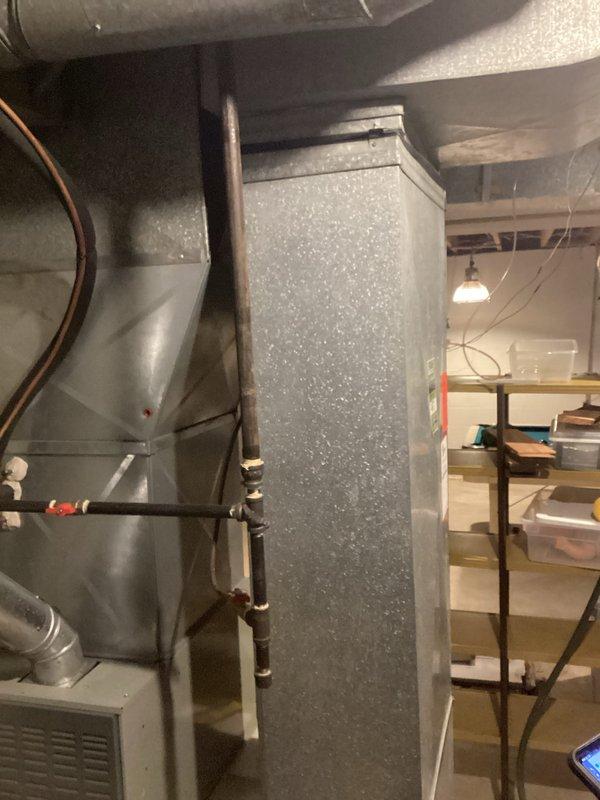 Completed comprehensive HVAC system assessment for residential air conditioning replacement in basement utility area. Documented existing furnace/air handler unit, ductwork configuration including main vertical plenum with gray textured finish, horizontal distribution ducts, and copper refrigerant lines. Photographed current equipment layout, mechanical room conditions, and accessibility for replacement installation planning.