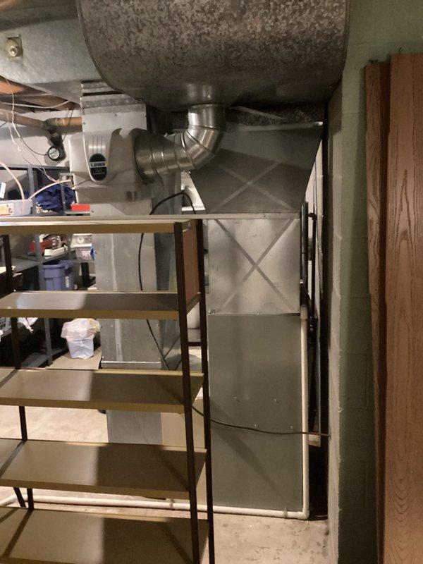 Completed comprehensive HVAC system assessment for residential air conditioning replacement in basement utility area. Documented existing furnace/air handler unit, ductwork configuration including main vertical plenum with gray textured finish, horizontal distribution ducts, and copper refrigerant lines. Photographed current equipment layout, mechanical room conditions, and accessibility for replacement installation planning.