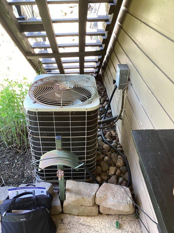 Conducted comprehensive site assessment of existing outdoor air conditioning condenser unit for full system replacement estimate. Unit showed significant weathering and discoloration, indicating age-related deterioration. Evaluated current installation including electrical connections, refrigerant line set configuration, condensate drainage system with white PVC piping and purple-primed joints, and existing concrete pad foundation. Documented equipment specifications, existing ductwork connections, and all associated plumbing and electrical components. Photographed unit positioning under pergola structure, clearance requirements, and surrounding landscape features including decorative rock border. Assessed accessibility for replacement equipment installation and verified electrical service panel location for proper disconnect sizing.