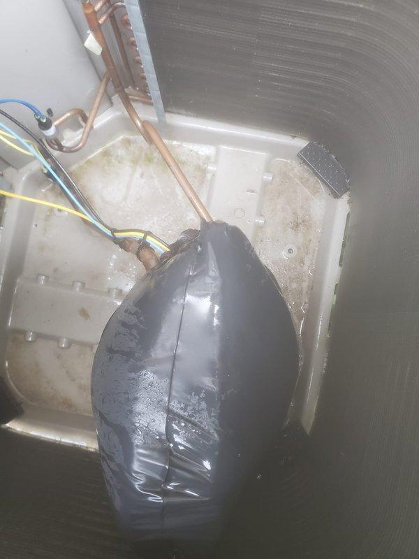Completed routine AC maintenance on residential split-system cooling unit. Inspected outdoor condenser unit positioned on composite pad adjacent to building structure, verified proper clearances and airflow around cabinet, and confirmed white PVC refrigerant lines and electrical conduit connections were secure. Examined interior evaporator coil assembly and drain pan for proper operation, noting active condensation present indicating system was cycling normally. Observed moisture accumulation in black plastic drain pan with visible water droplets on surfaces, confirmed drainage pathways were clear, and verified copper refrigerant lines showed no signs of damage or refrigerant leakage. Checked evaporator coil fins for debris accumulation and airflow restrictions. All components inspected and found to be operating within normal parameters for continued reliable cooling performance.