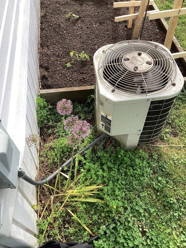 Responded to service call for non-functional air conditioning system at mobile home residence. Evaluated existing outdoor condenser unit of undetermined age with cylindrical design and beige casing, noting furnace had been previously replaced while AC unit remained original. Unit located on ground level adjacent to house siding with electrical disconnect box and conduit visible. Documented equipment condition and installation site through photographs showing condenser positioning, electrical connections, and surrounding landscaping. Provided customer with estimate for complete AC system replacement to restore cooling functionality.