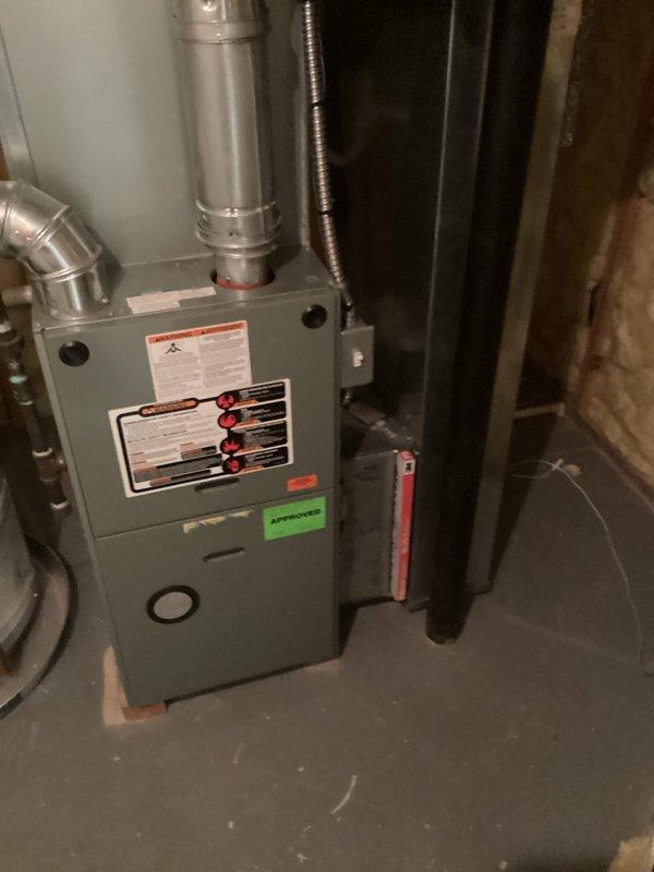 Conducted comprehensive site assessment of existing residential HVAC system located in basement mechanical room to provide full system replacement estimate. Evaluated current gray metal furnace unit with vertical flue pipe configuration, connected ductwork system including silver galvanized supply ducts with elbow joints, and accompanying air handler equipment. Documented equipment specifications from manufacturer labels and technical plates on furnace front panel. Assessed ductwork routing and connections, flexible conduit runs, and overall system layout within unfinished basement space with exposed framing. Photographed existing installation including furnace positioning on concrete floor, vertical and horizontal duct configurations, and proximity to adjacent water heating equipment. Evaluated accessibility for potential equipment replacement and noted existing ventilation system connections. Measured available space parameters for new equipment installation considerations and review