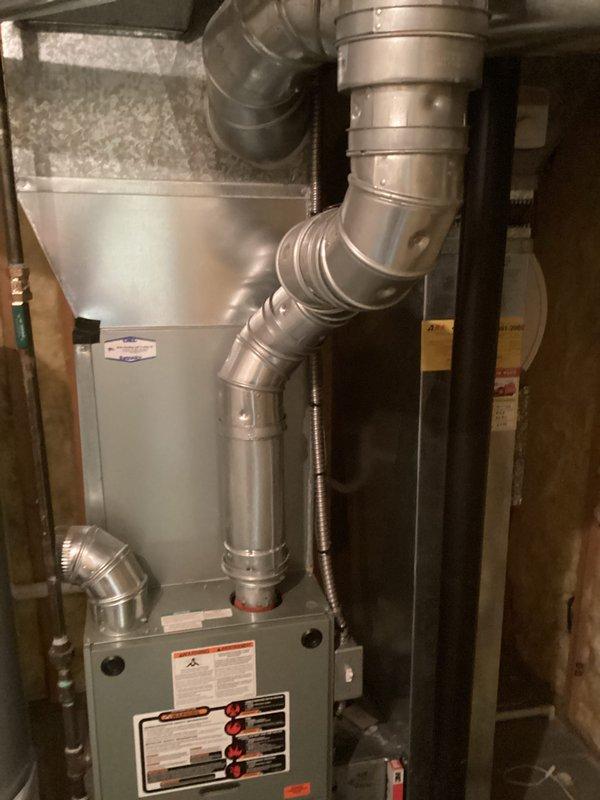 Conducted comprehensive site assessment of existing residential HVAC system located in basement mechanical room to provide full system replacement estimate. Evaluated current gray metal furnace unit with vertical flue pipe configuration, connected ductwork system including silver galvanized supply ducts with elbow joints, and accompanying air handler equipment. Documented equipment specifications from manufacturer labels and technical plates on furnace front panel. Assessed ductwork routing and connections, flexible conduit runs, and overall system layout within unfinished basement space with exposed framing. Photographed existing installation including furnace positioning on concrete floor, vertical and horizontal duct configurations, and proximity to adjacent water heating equipment. Evaluated accessibility for potential equipment replacement and noted existing ventilation system connections. Measured available space parameters for new equipment installation considerations and review