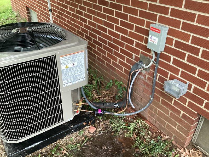 Completed installation of new Bryant air conditioning condenser unit at residential property. Mounted unit on composite base pad against exterior brick wall in side yard location. Installed electrical disconnect box on brick wall above unit with proper conduit routing. Ran refrigerant lines with black foam insulation from condenser up exterior wall, securing lines with appropriate fittings and service ports. Installed condensate pump with discharge line routed to exterior per sales specifications. Verified all electrical connections, tested system operation, and confirmed proper refrigerant charge levels.