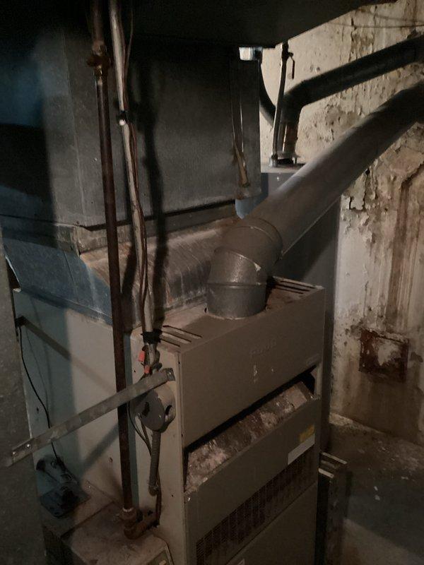 Completed estimate for replacement of 25-year-old residential air conditioning system. Evaluated existing outdoor condenser unit located in side yard utility area against brick building, noting aged equipment mounted on concrete pad with refrigerant line set penetrating exterior wall. Assessed indoor furnace and air handler system in basement to determine compatibility requirements for new equipment installation. Documented current system configuration including electrical service, disconnect location, and existing ductwork connections. Provided comprehensive replacement options for complete HVAC system upgrade to improve efficiency and reliability.