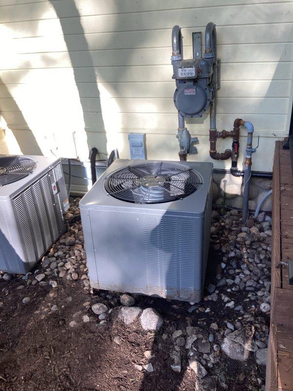 Conducted HVAC estimate for air conditioning replacement at residential property with two outdoor condenser units positioned against exterior wall on gravel base. Upon inspection, discovered one unit was low on refrigerant. Recharged the system with appropriate refrigerant to restore proper operating levels. Documented existing dual-unit installation including positioning relative to gas meter infrastructure and building utilities for replacement planning purposes.
