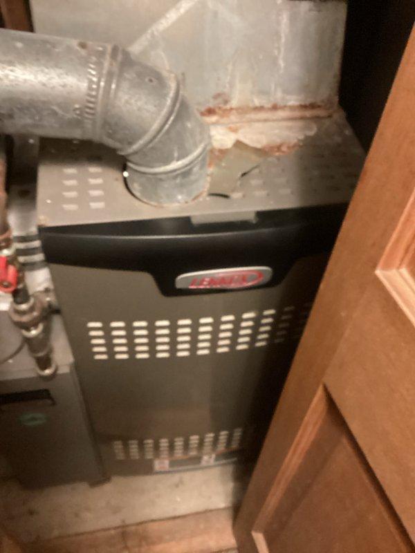 Conducted comprehensive assessment of existing residential HVAC system for furnace replacement estimate. Documented current black furnace unit installed in confined utility space with connected silver galvanized ductwork, air handler with humidifier attachment, and associated condensate drainage system. Noted rust discoloration on vertical duct connections and drain pan, copper and PVC piping configuration, and overall equipment layout within tight mechanical closet. Photographed complete system including ductwork transitions, plumbing connections with shutoff valves, and spatial constraints for replacement planning purposes.