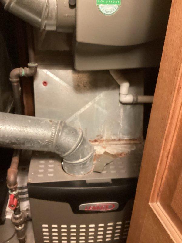 Conducted comprehensive assessment of existing residential HVAC system for furnace replacement estimate. Documented current black furnace unit installed in confined utility space with connected silver galvanized ductwork, air handler with humidifier attachment, and associated condensate drainage system. Noted rust discoloration on vertical duct connections and drain pan, copper and PVC piping configuration, and overall equipment layout within tight mechanical closet. Photographed complete system including ductwork transitions, plumbing connections with shutoff valves, and spatial constraints for replacement planning purposes.
