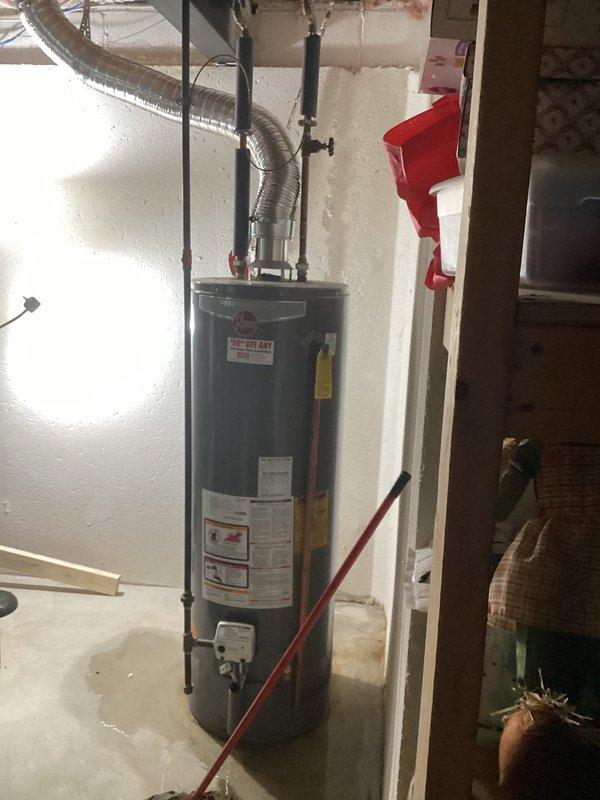 Responded to service call for leaking water heater in unfinished basement with walk-out access. Inspected 10-year-old residential water heater unit showing signs of active leak at base, with visible moisture staining on concrete floor. Documented existing installation including top-mounted plumbing connections, pressure relief valve, copper supply lines, flexible vent ductwork, and safety strapping. Photographed unit specifications, manufacturer labels, and overall condition to prepare replacement estimate as requested.