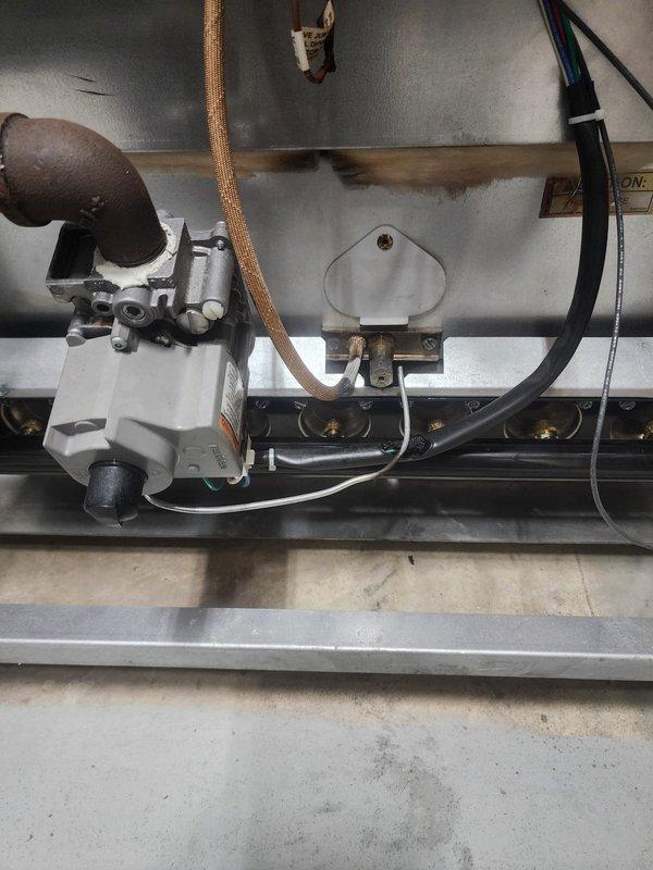 Responded to system shutdown initiated by utility company due to gas leak detected at burner assembly. Upon arrival, inspected furnace combustion chamber and identified leak at burner manifold connections. Photographed gas valve assembly, heat exchanger condition showing soot patterns and discoloration, and burner rail with brass orifices. Documented electrical connections, ignition components, and copper ground wire routing during inspection. System remains offline pending leak repair and utility company clearance for restart.