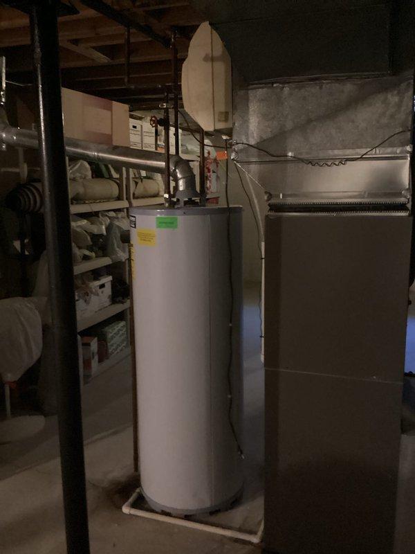 Technician responded to provide a humidifier estimate and identified an aging water heater requiring replacement. Documented the existing water heater installation in the basement utility area, noting the unit's condition and configuration alongside the HVAC system. Prepared comprehensive estimate for water heater replacement to address equipment age and prevent potential failure.